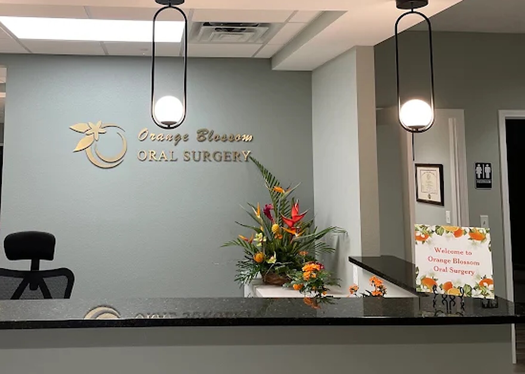 The Orange Blossom Oral Surgery reception desk, with the practice name in gold lettering on a sage green wall and fresh flowers on the counter