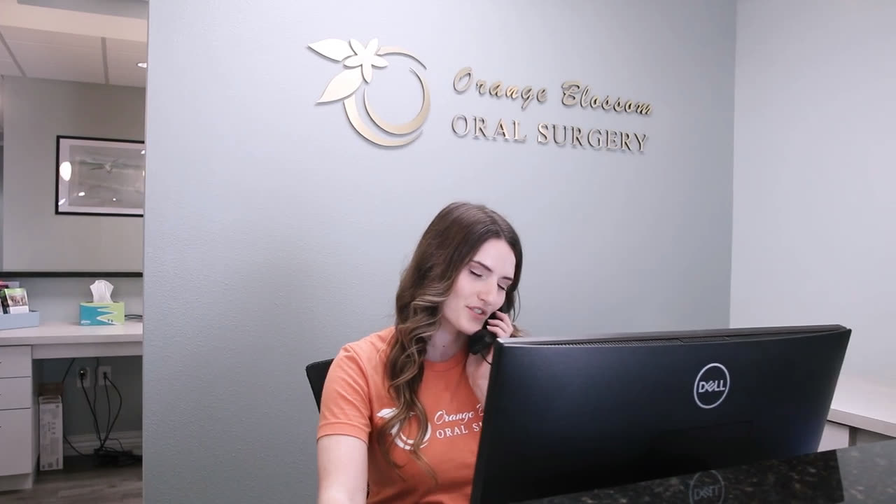An Orange Blossom team member taking a patient call at the front desk, under the practice sign